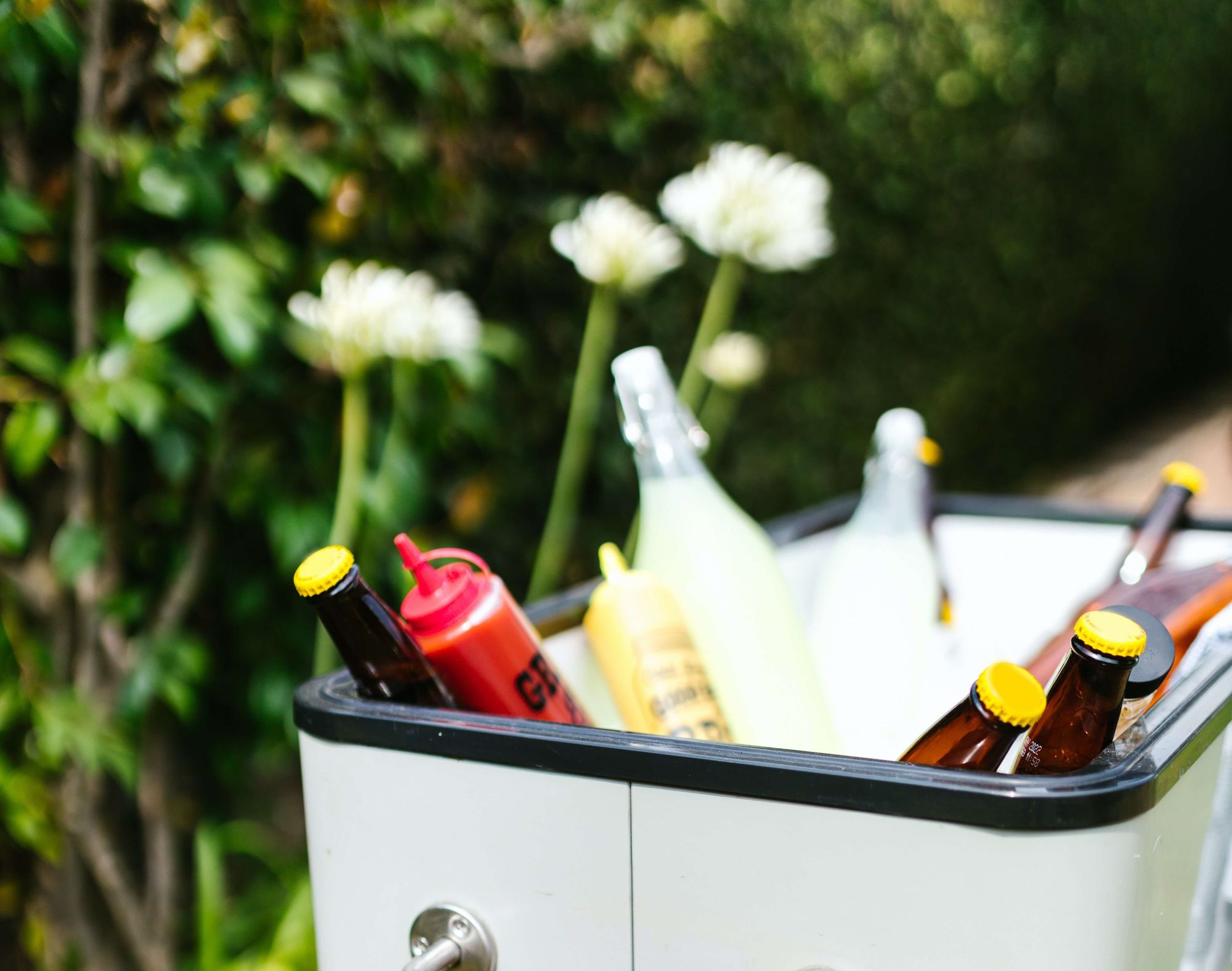 An open cooler outside with various drinks and condiments.
