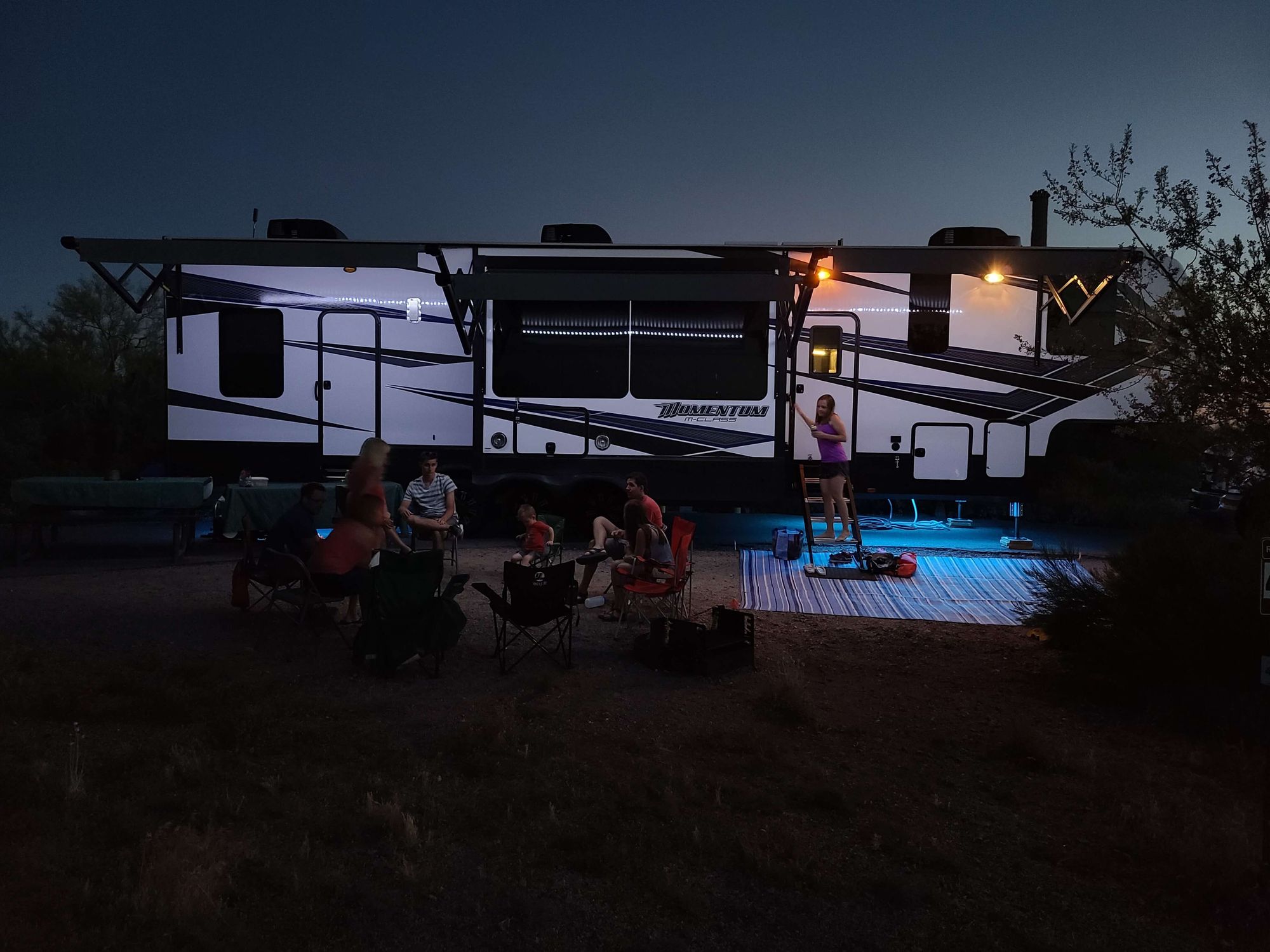 A large trailer with a family sitting together outside at night.