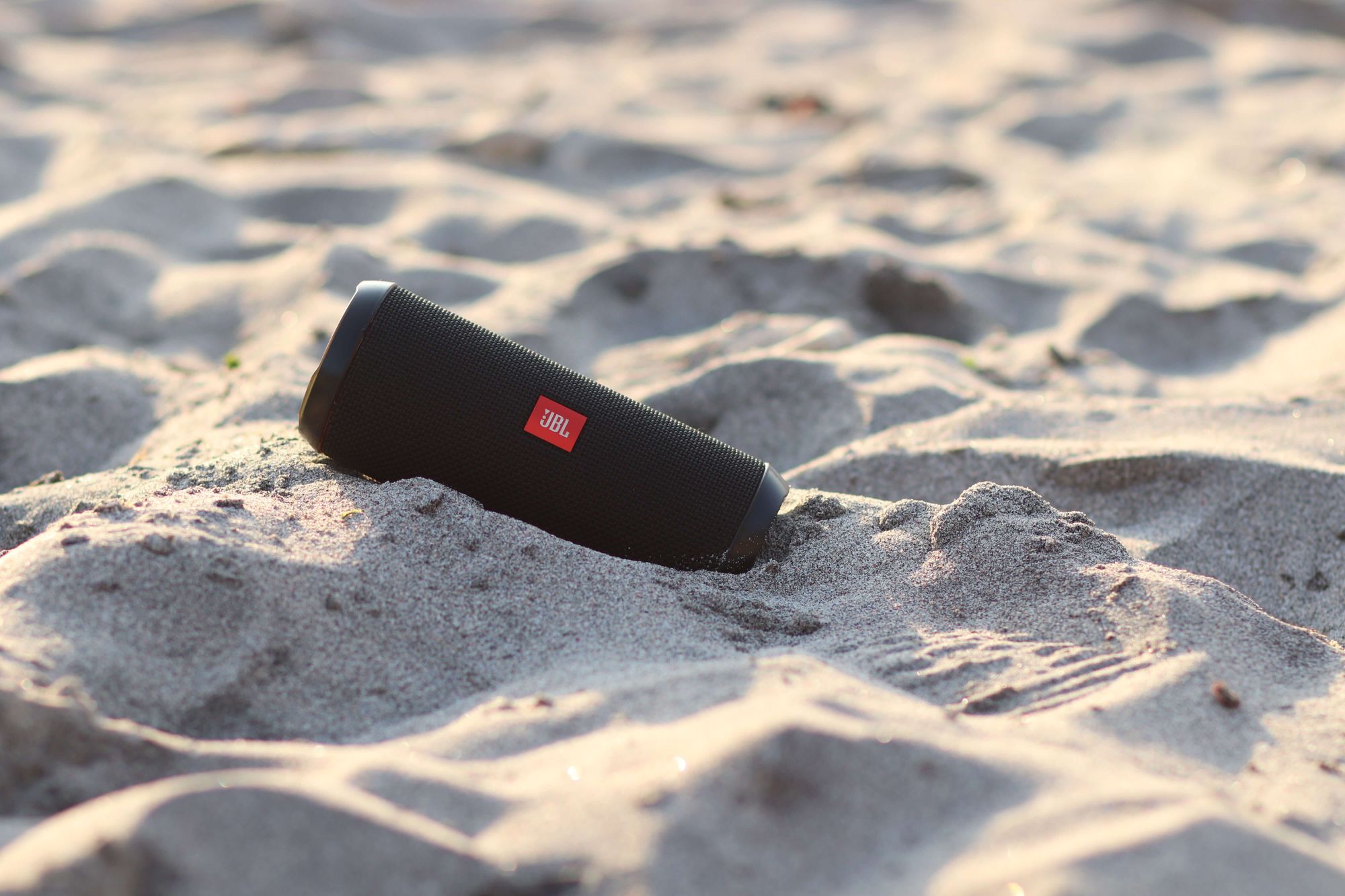 A portable speaker on sandy ground.