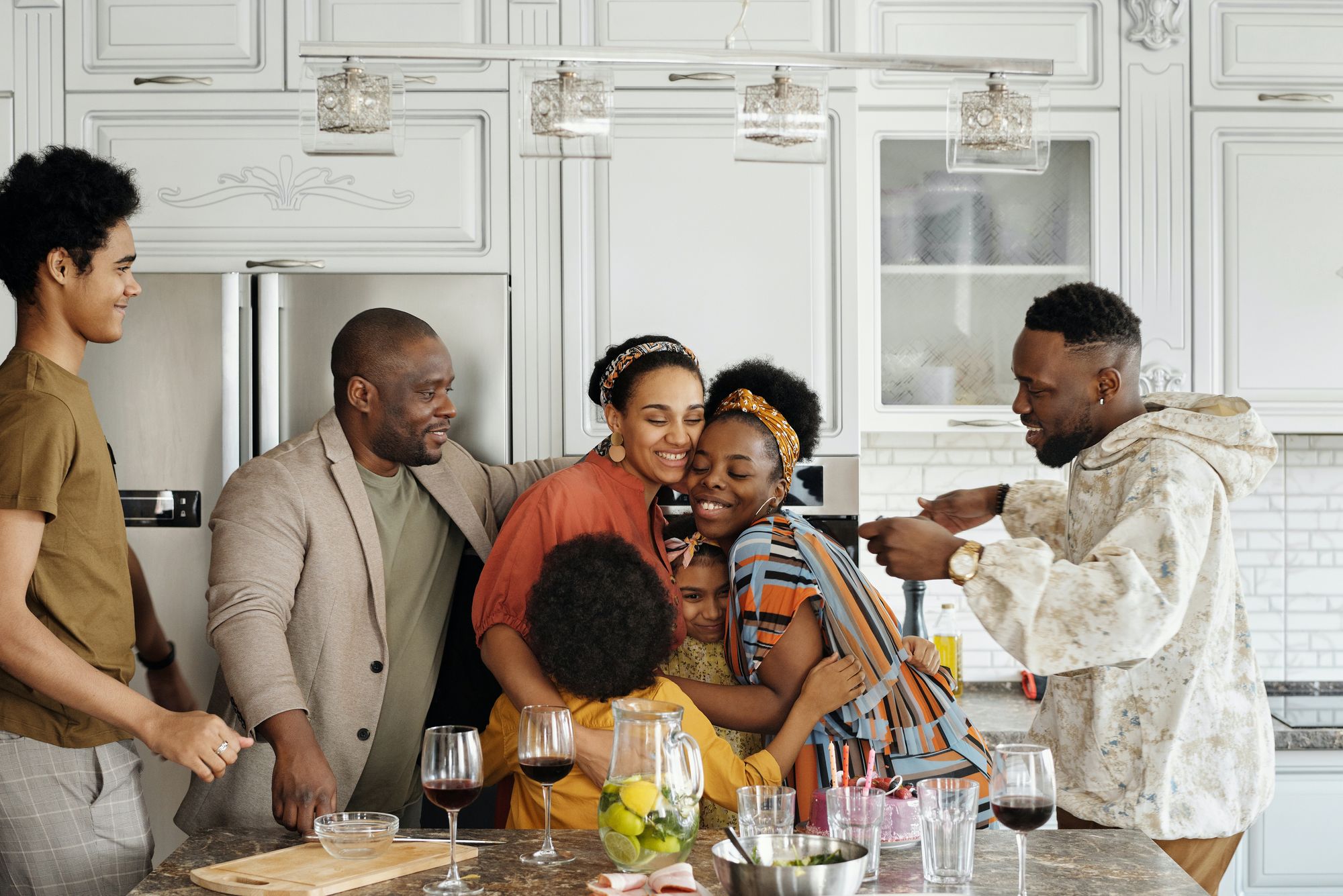 A family in a kitchen, hugging and smiling, gathering for a meal.