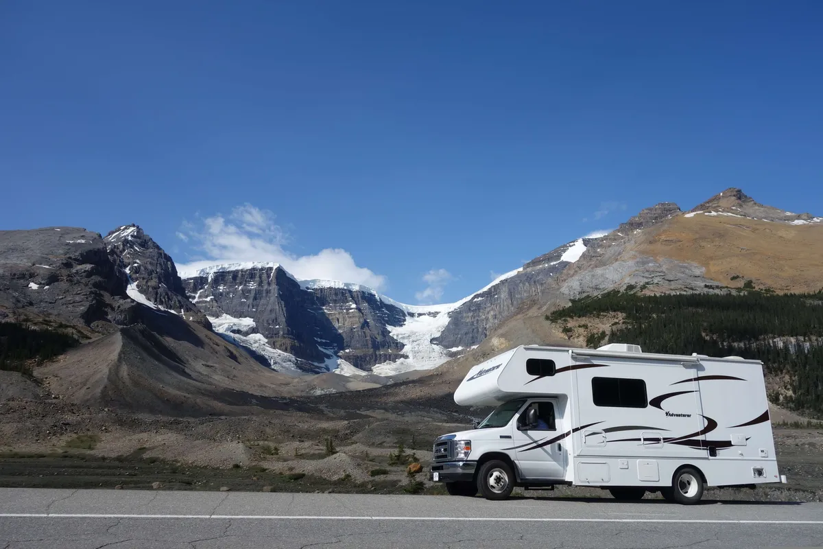 An RV parked alongside a highway in Canada, with rolling hills covered in snow in the background.