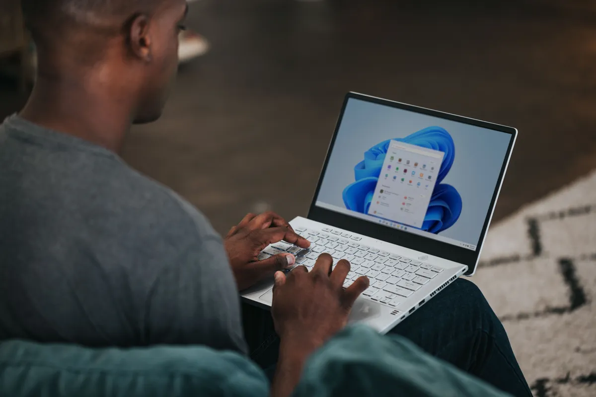A man using a laptop opening the Start Menu on Windows 11.