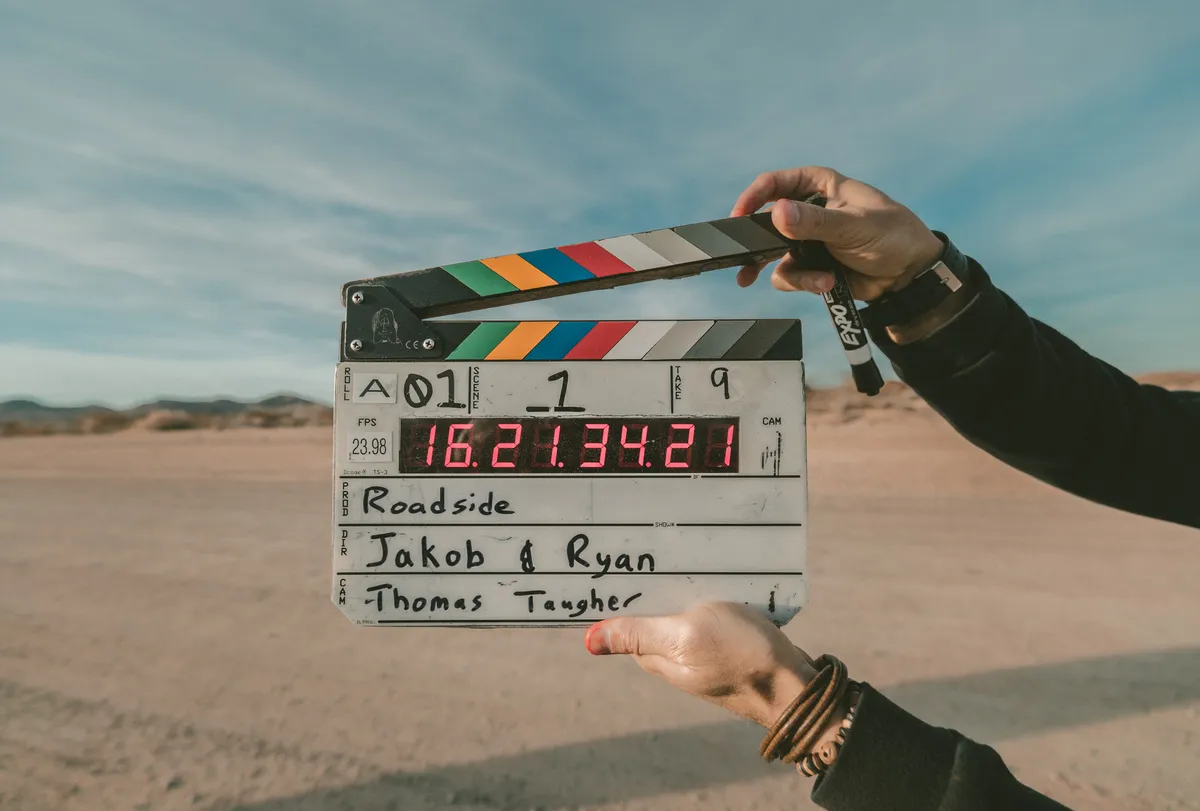 A photo of hands holding a clapperboard on an outdoor set.