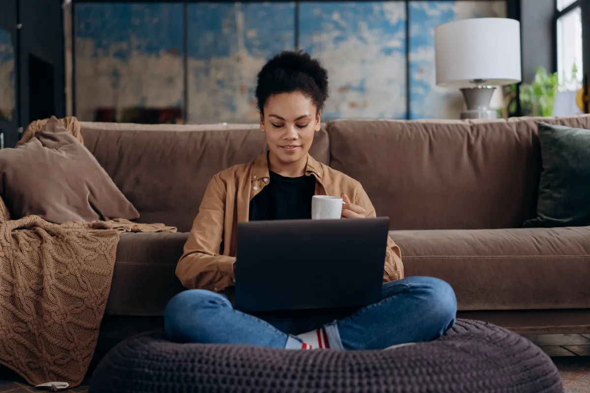 A woman sitting on a bean bag chair with her laptop and holding a mug.